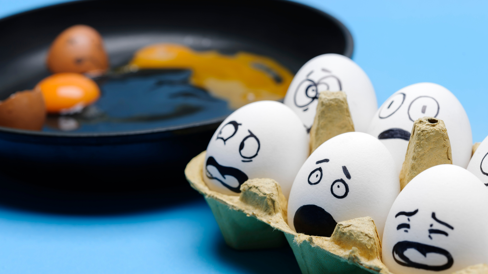 Eggs next to a frying pan with fearful expressions drawn on their shells.