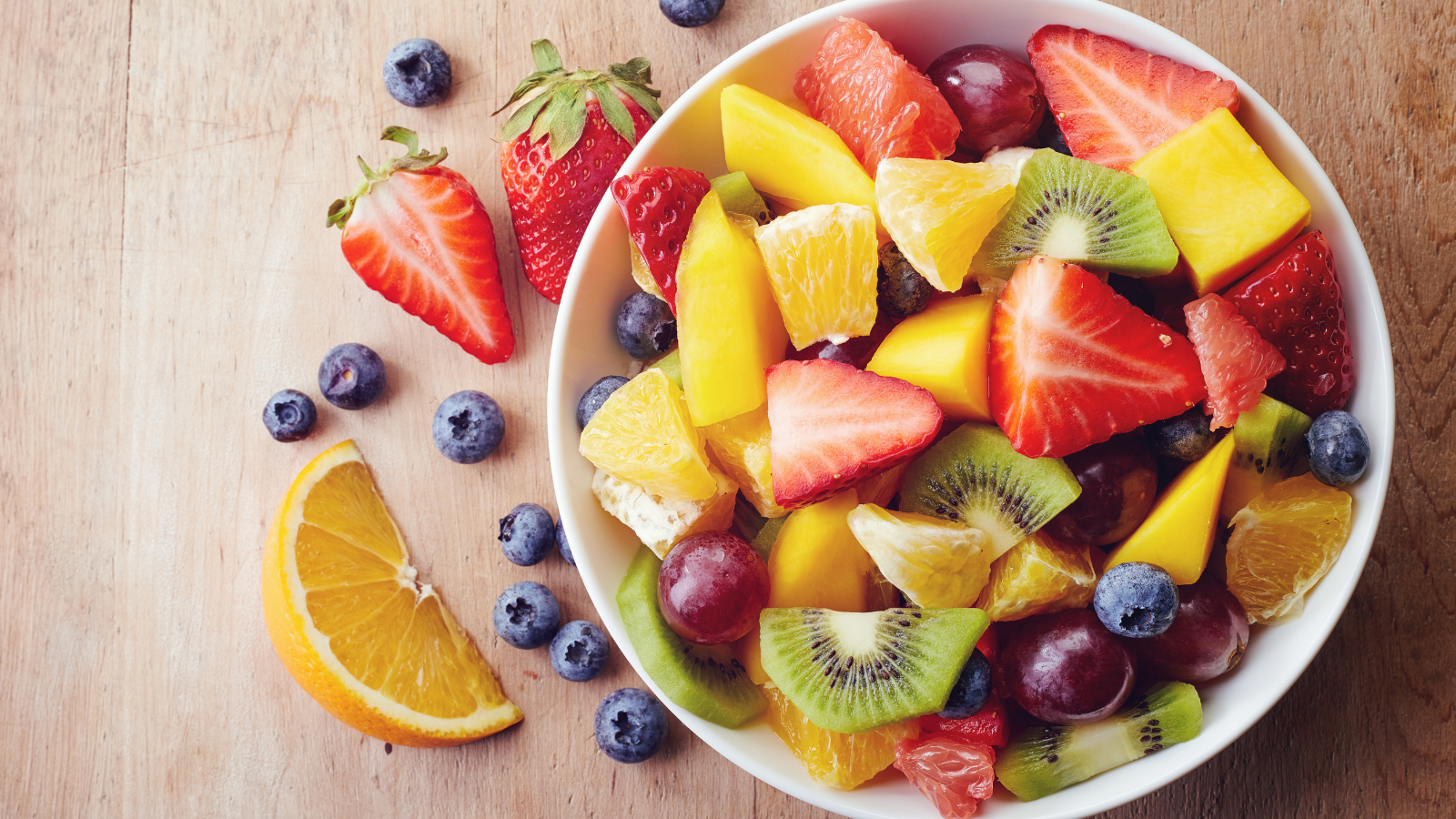 A bowl of fresh fruit, including halved strawberries, blueberries, kiwi, and orange slices.