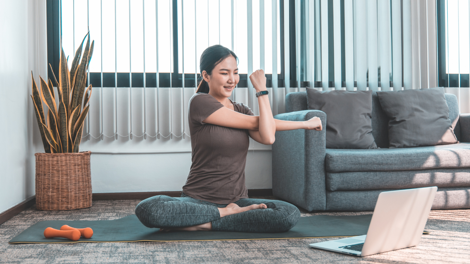 Asian woman doing stretches on a mat in front of her laptop.