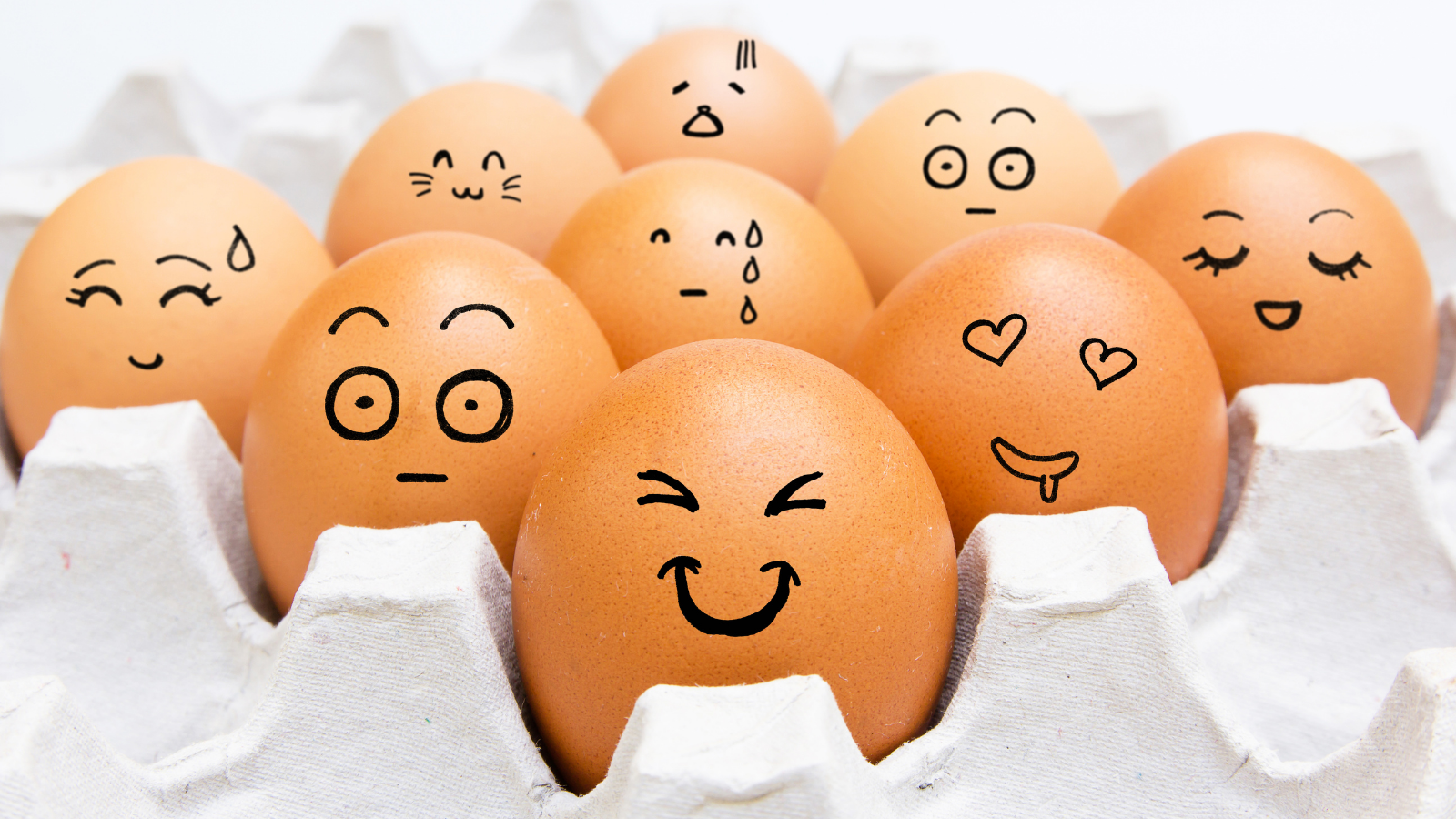 A carton of chicken eggs with emojii expressions drawn on the shells.