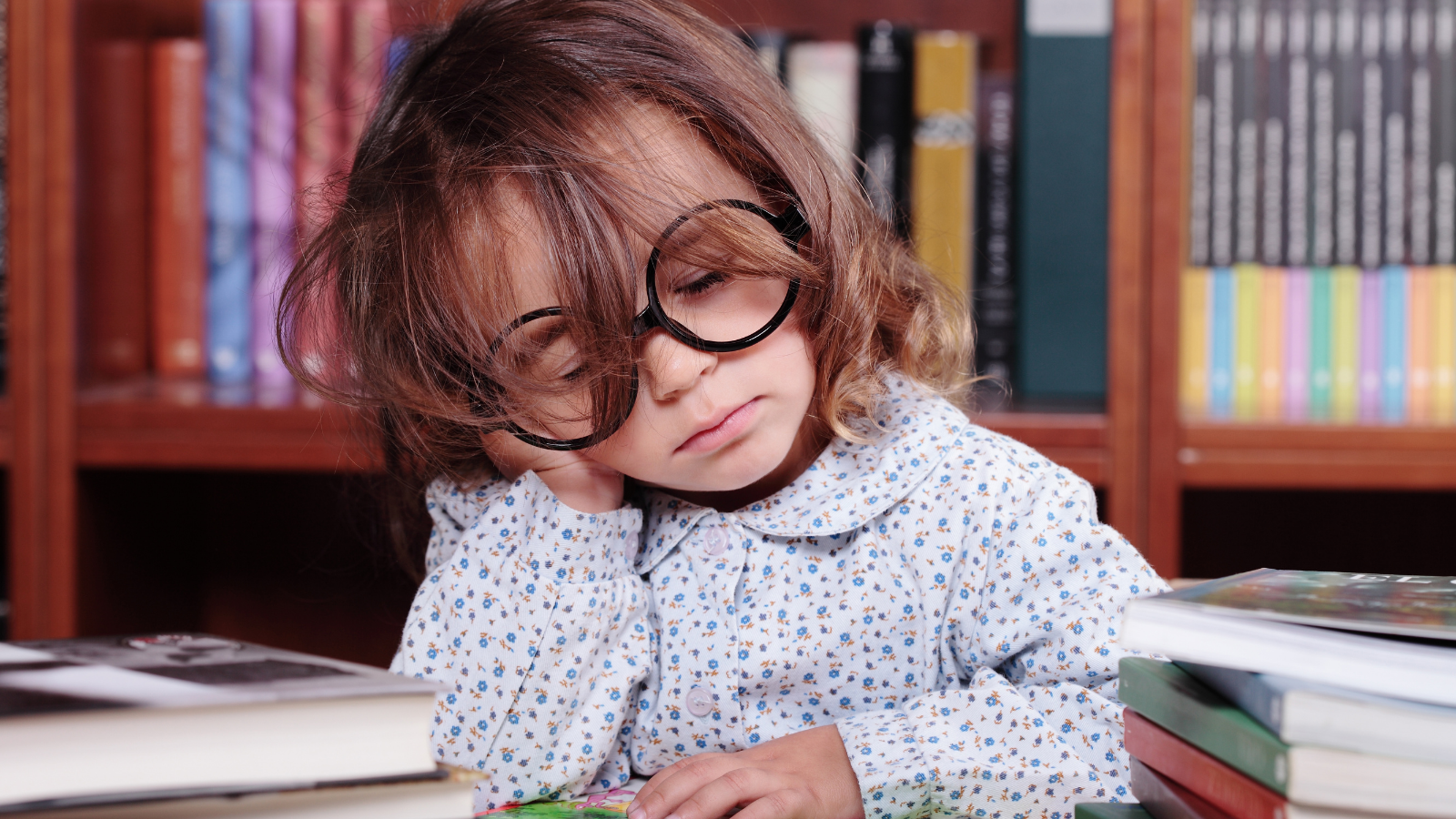 Young girl wearing glasses, at a library falling asleep.