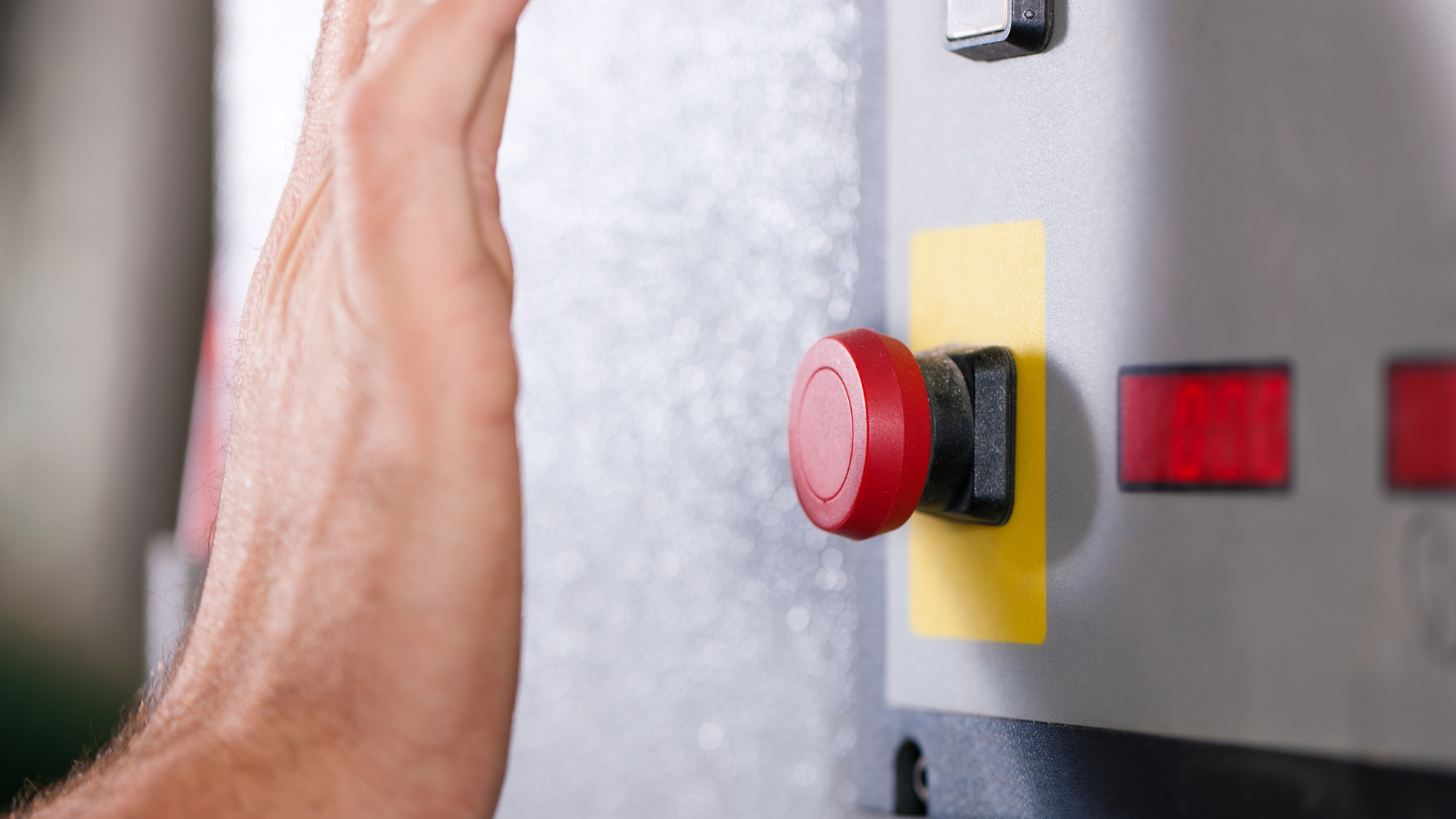 Hand hovering over a red button on the wall.