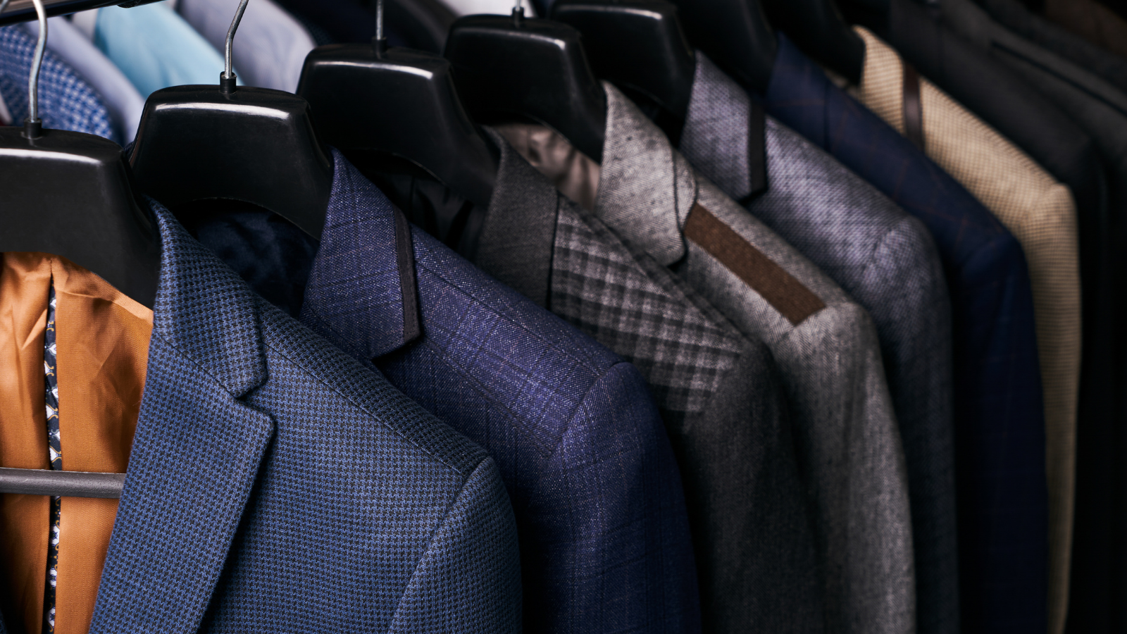 Suits of various colors and fabrics displayed on hangers.