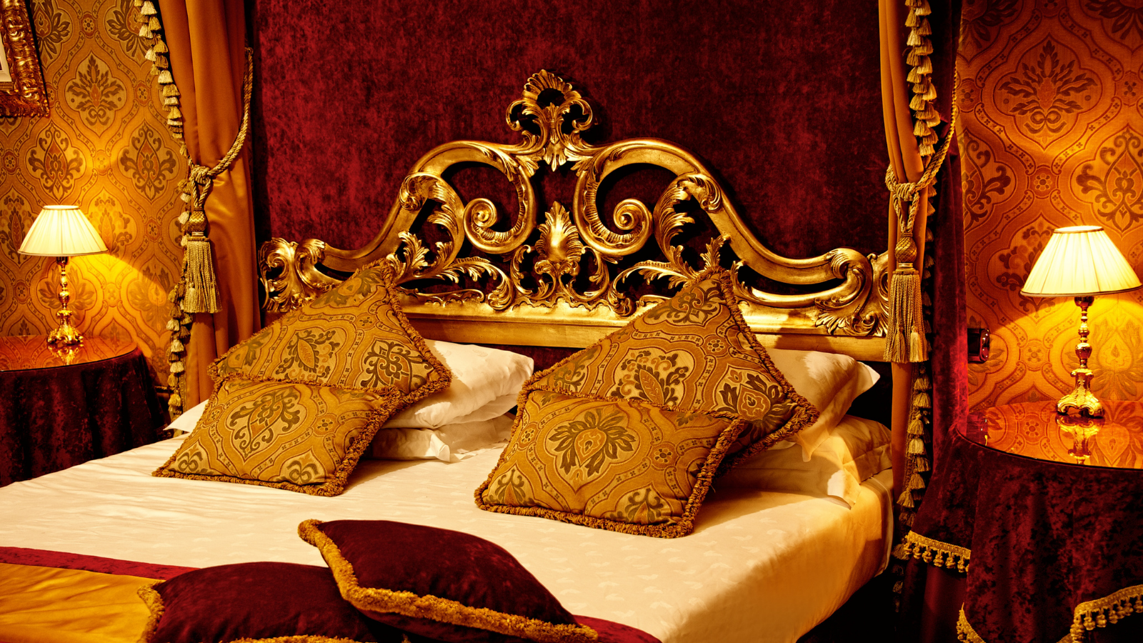 A luxurious bed with brocade and velvet bedding and a gold bedframe.